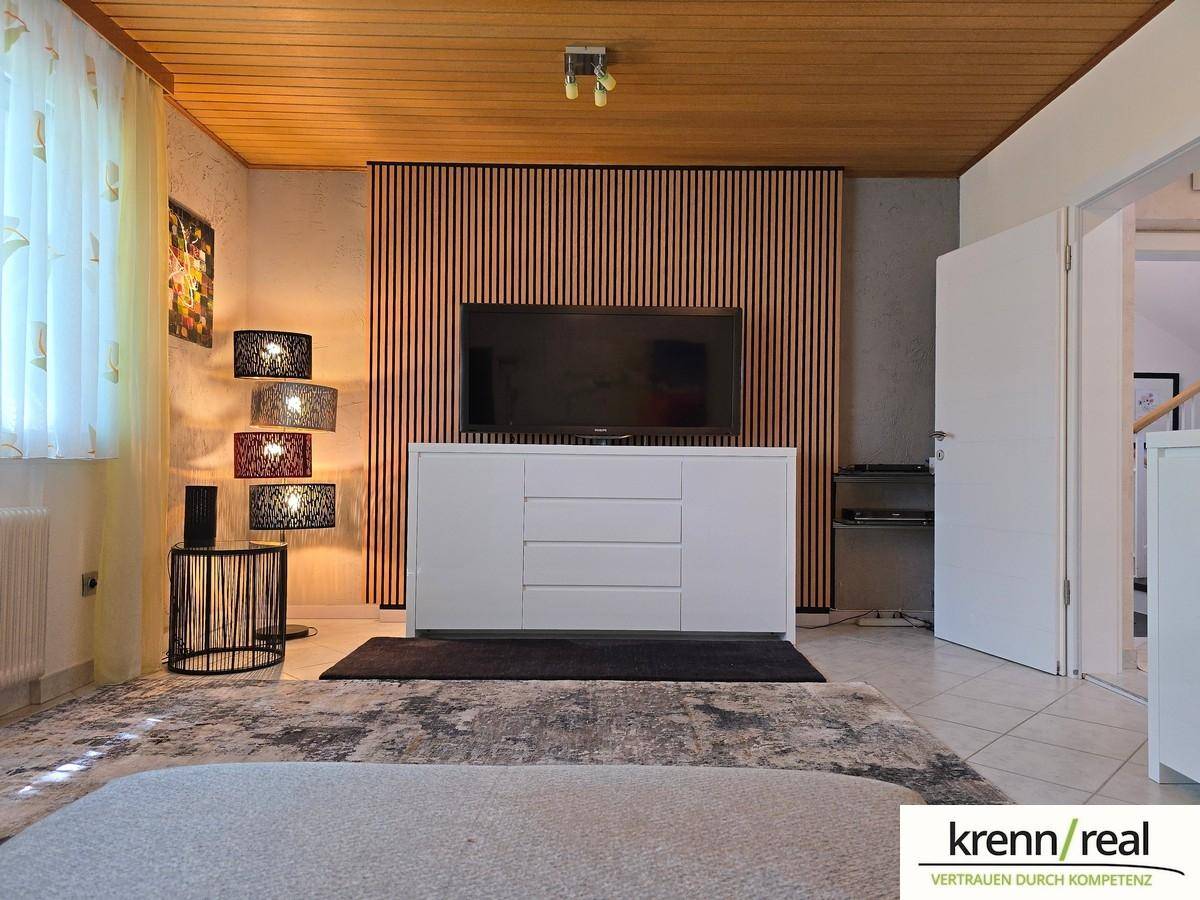 Wohnzimmer mit Holzakzentwand, Fliesenboden und moderner Kommode.