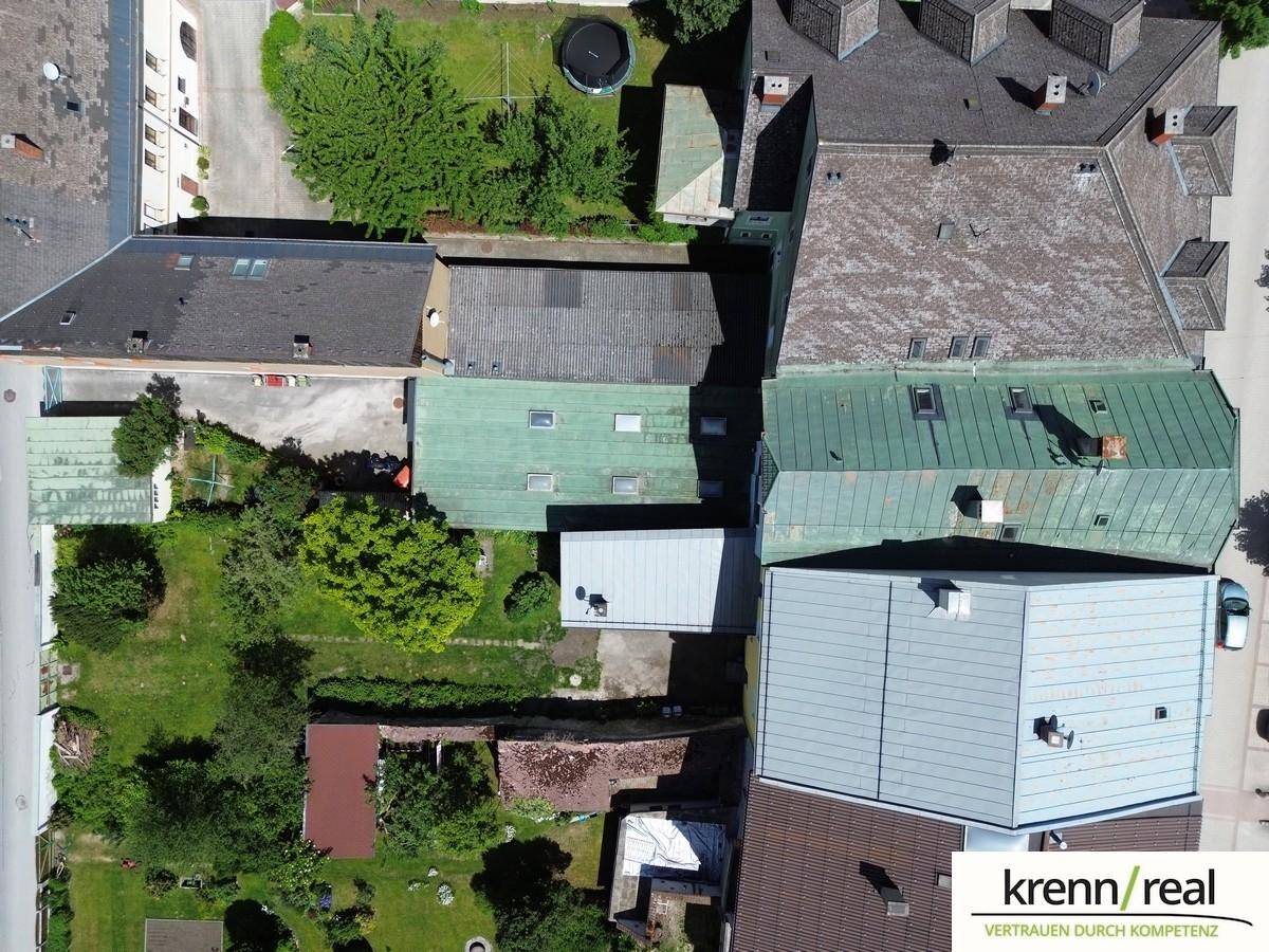 Draufsicht aus der Vogelperspektive auf Dächer, Hinterhöfe und Gärten mehrerer Gebäude in einer städtischen Umgebung.