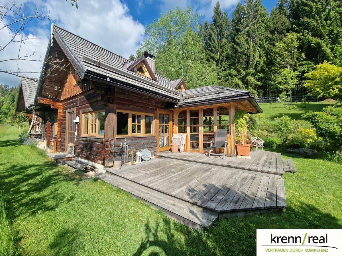 Rustikale Holzterrasse am Haus, umgeben von grüner Wiese und Wald, mit Sitzgelegenheiten.
