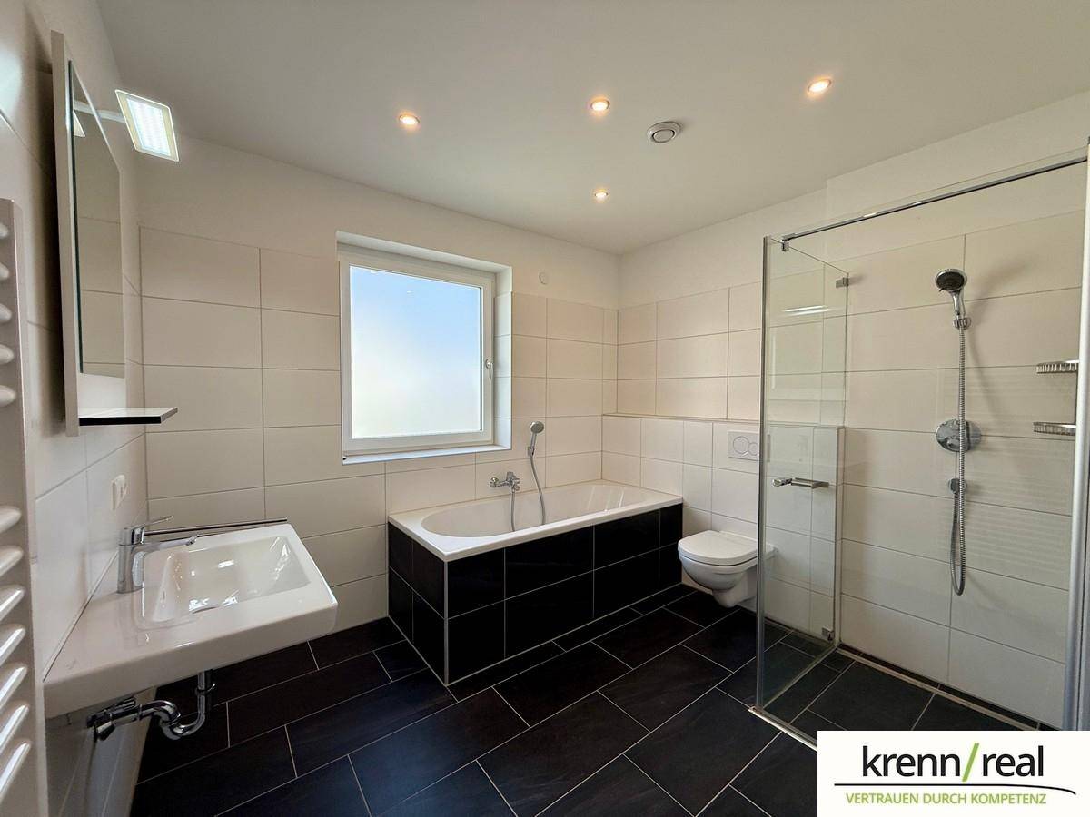 Modernes Badezimmer mit Badewanne, Dusche, WC und Fenster für Tageslicht.