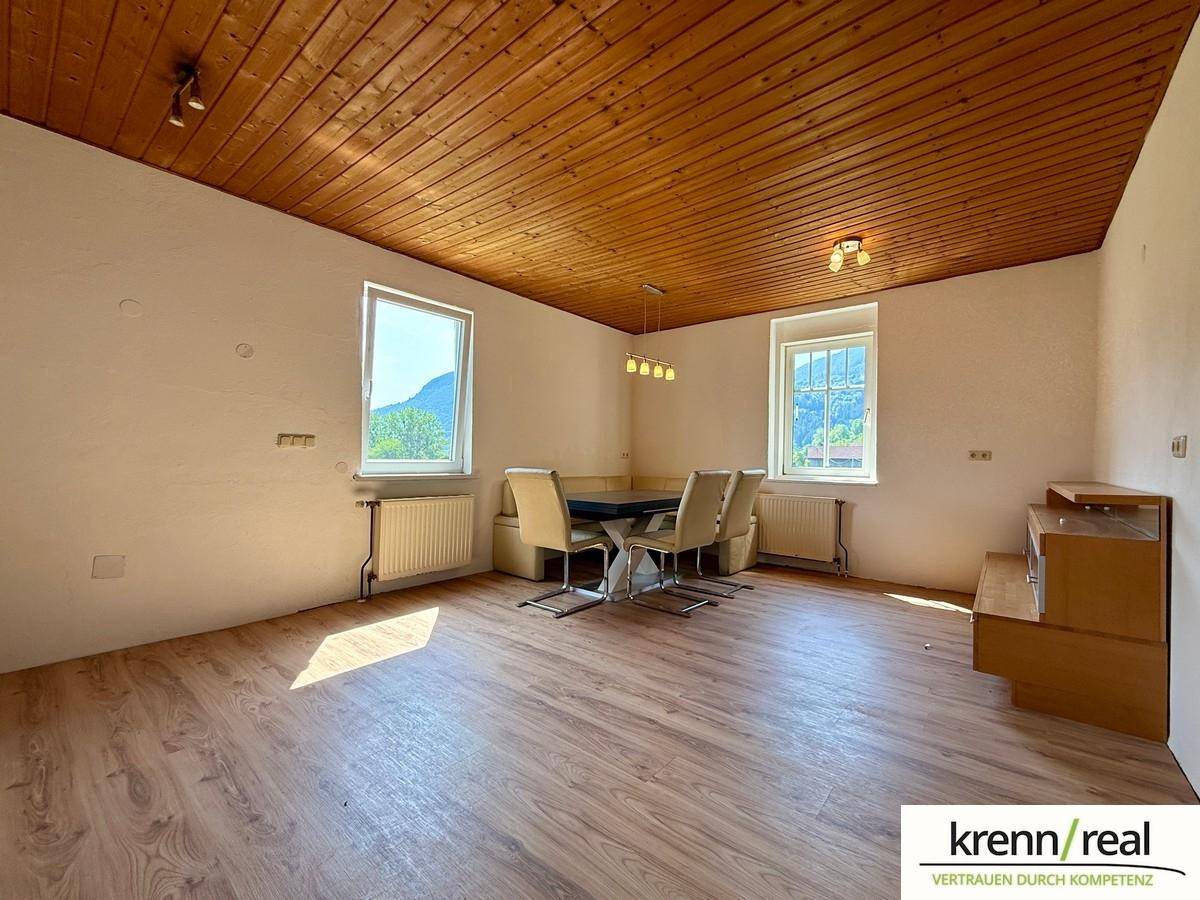 Heller Essbereich mit Holzbalkendecke, Laminatboden und Blick auf die grüne Landschaft durch die Fenster.