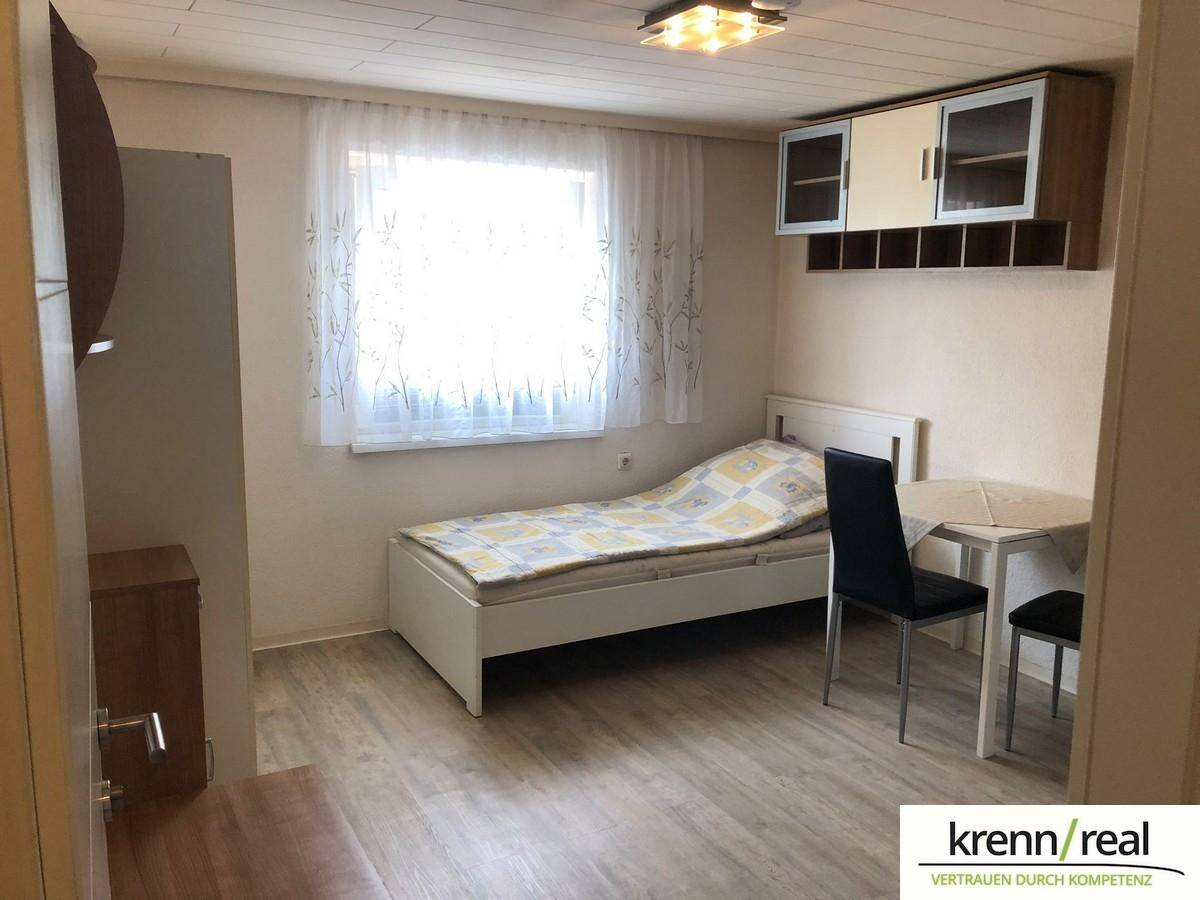 Gemütliches Schlafzimmer mit Einzelbett, Esstisch und Hängeschränken, beleuchtet durch ein großes Fenster.