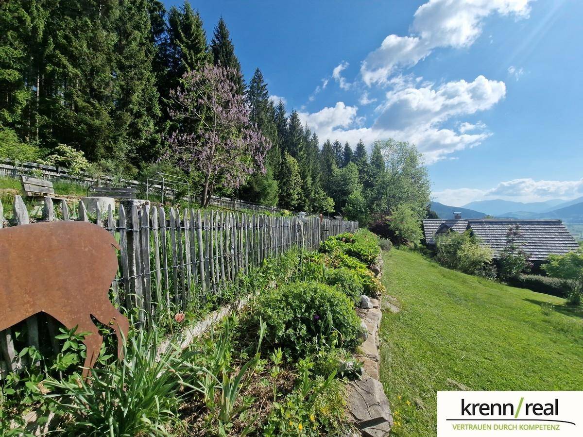 Rustikaler Holzzaun entlang eines blühenden Gartens mit Blick auf die Berglandschaft.