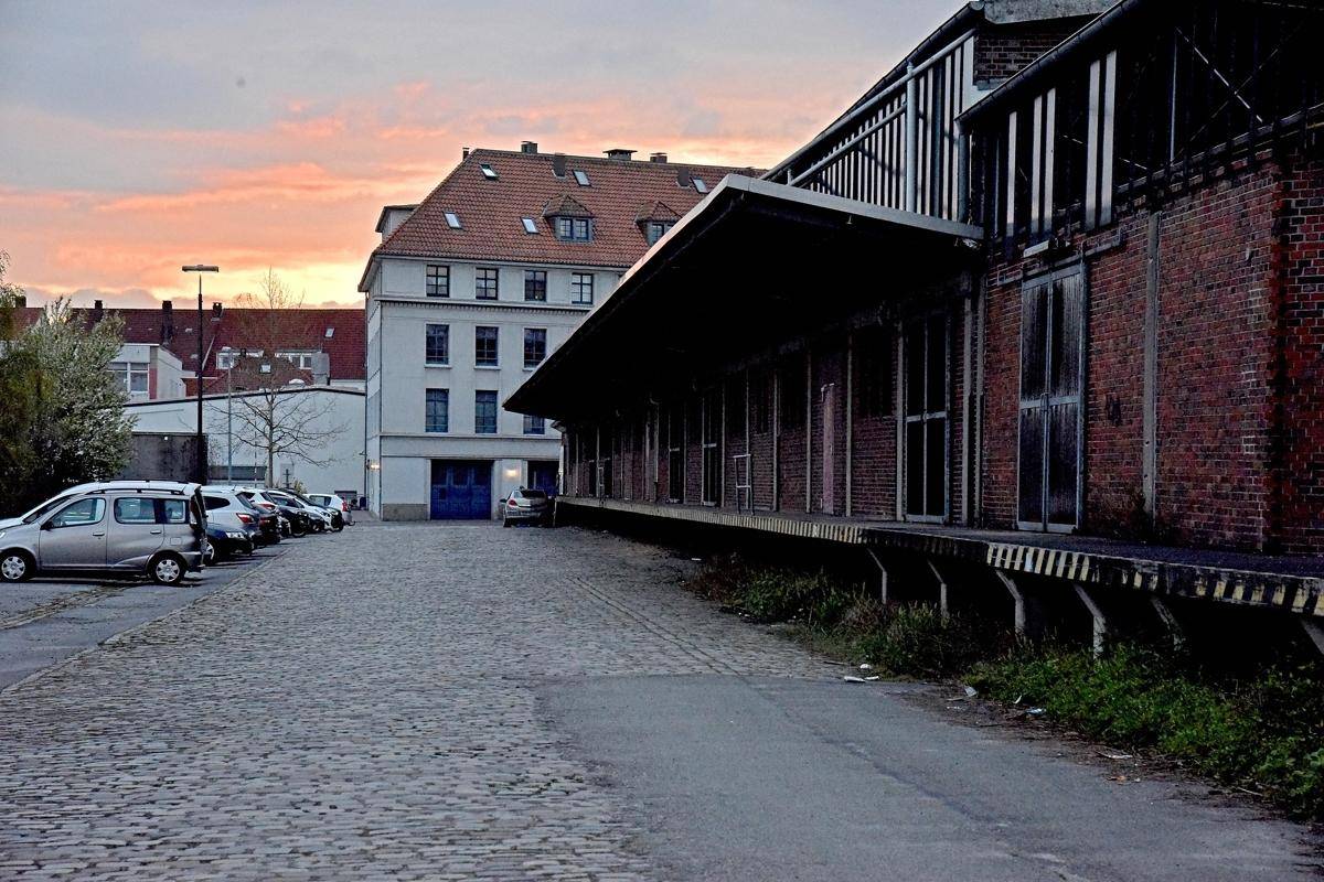 Industriegebäude mit Laderampen und Parkplatz bei Sonnenuntergang mit orangefarbenem Himmel.