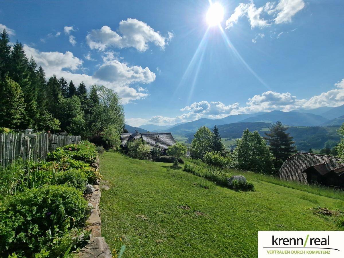Weitläufige grüne Landschaft mit sanften Hügeln und Bergen unter strahlend blauem Himmel.