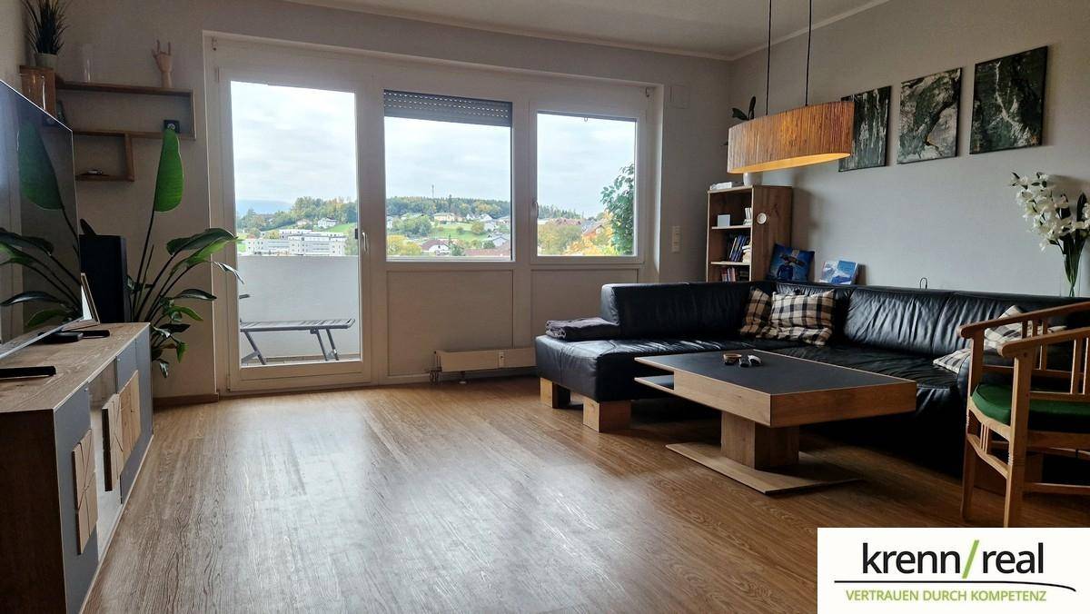 Helles Wohnzimmer mit Holzboden, großem Fenster und Zugang zum Balkon, bietet einen weiten Blick.
