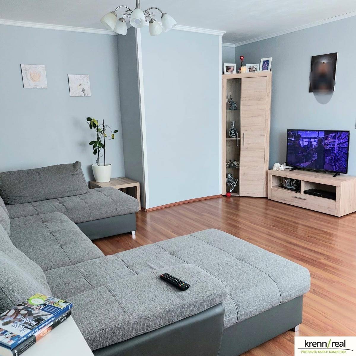 Gemütliches Wohnzimmer mit großem Ecksofa, Laminatboden und hellblauen Wänden.
