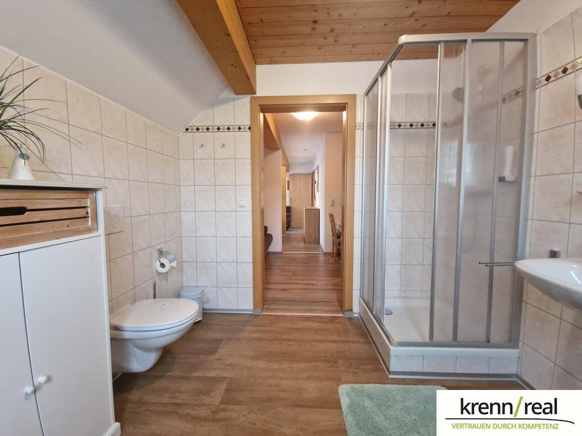 Gefliestes Badezimmer mit Dusche, WC und Waschbecken, durch einen Flur verbunden.