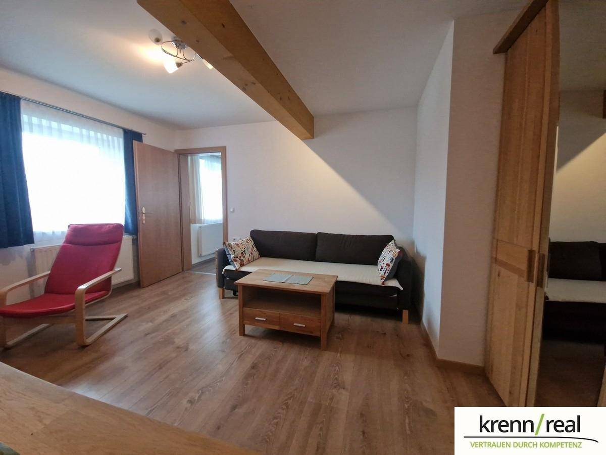 Heller Wohnbereich mit Holzbalken, bequemer Couch und einem roten Sessel, bietet Platz zum Entspannen.