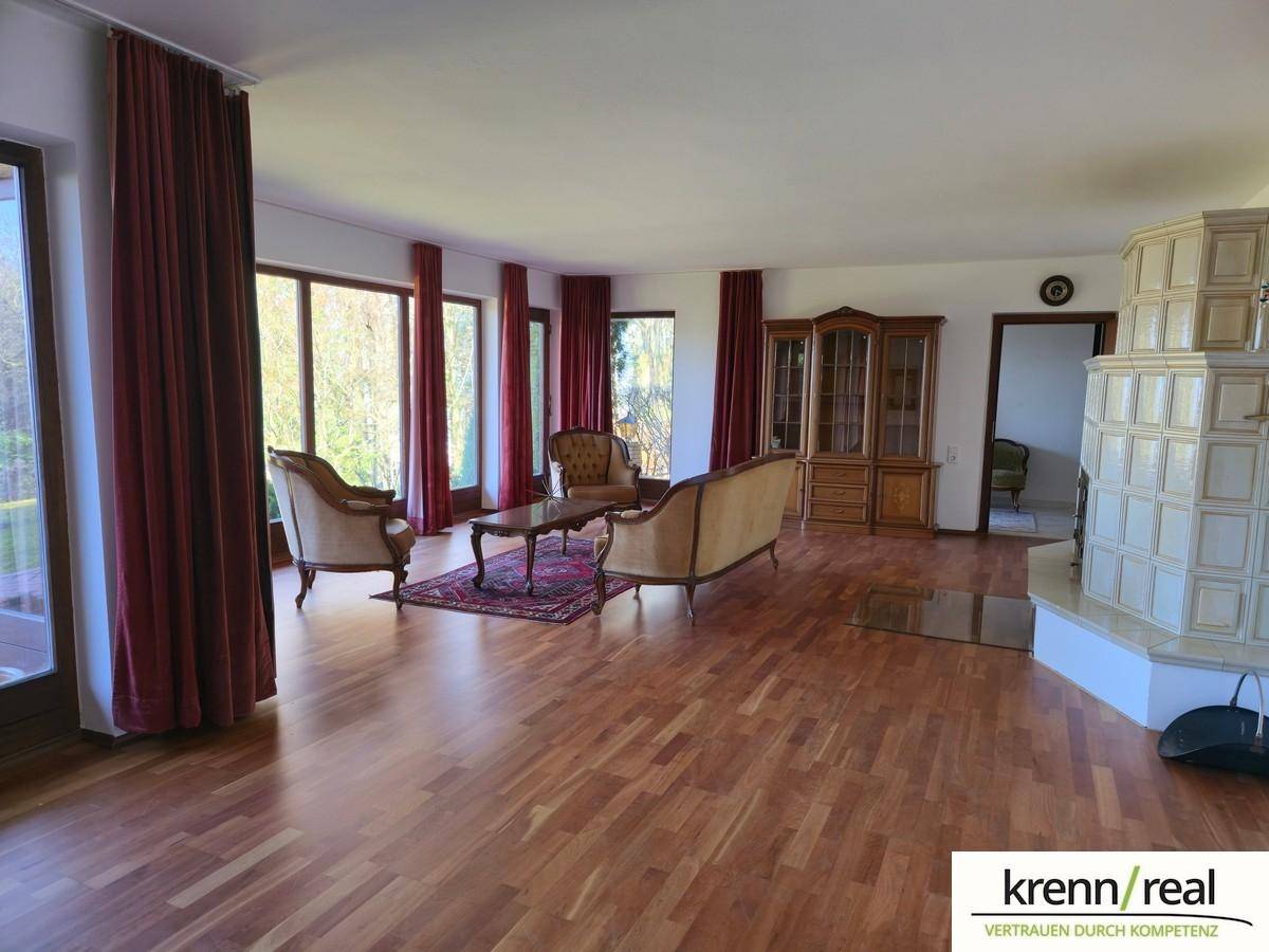 Helles Wohnzimmer mit Parkettboden, großen Fenstern und einem traditionellen Kachelofen.