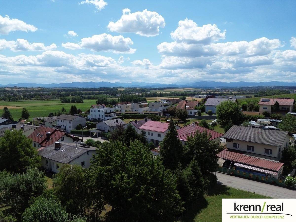 Weitläufige Wohnsiedlung mit grünen Feldern und Bergen im Hintergrund unter blauem Himmel.