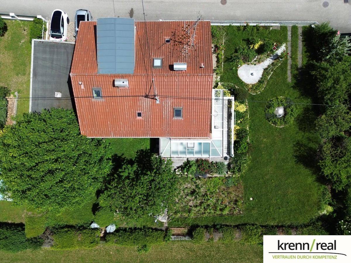 Vogelperspektive des Hauses mit rotem Ziegeldach, Gartenanlage und Solarmodulen auf dem Dach.