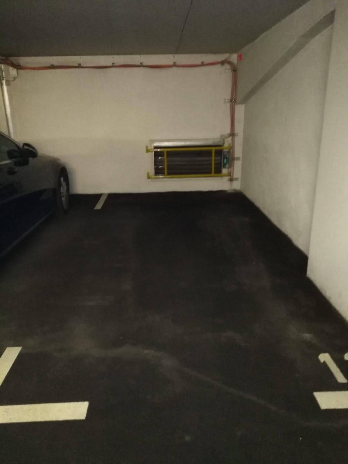 Tiefgaragenstellplatz mit dunklem Boden, weißen Markierungen und sichtbaren Installationen an der Wand.