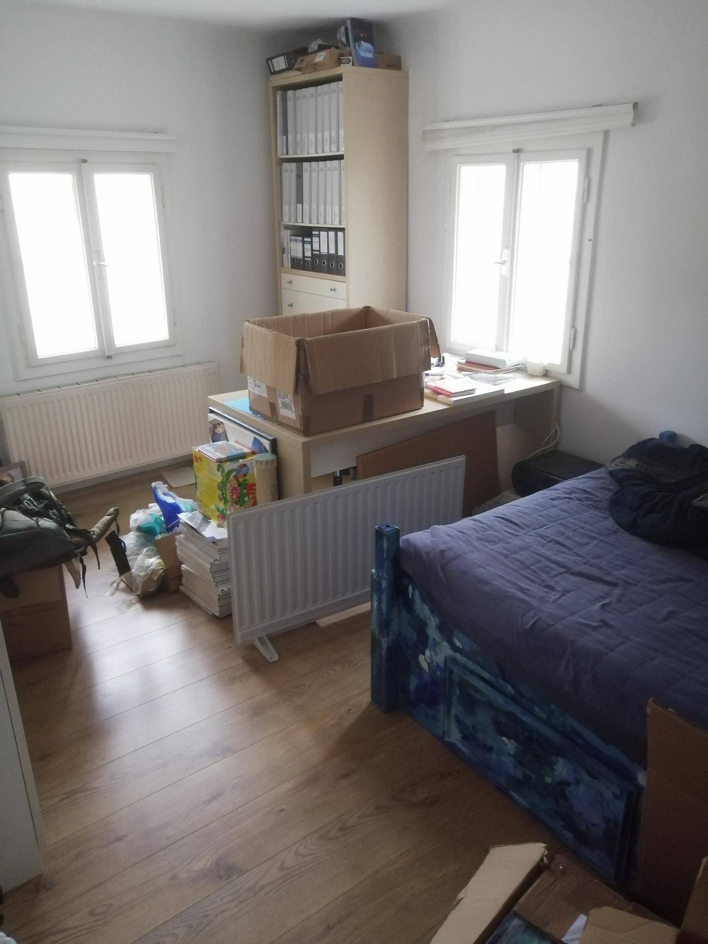 Schlafzimmer mit Bett, Schreibtisch und zwei Fenstern.