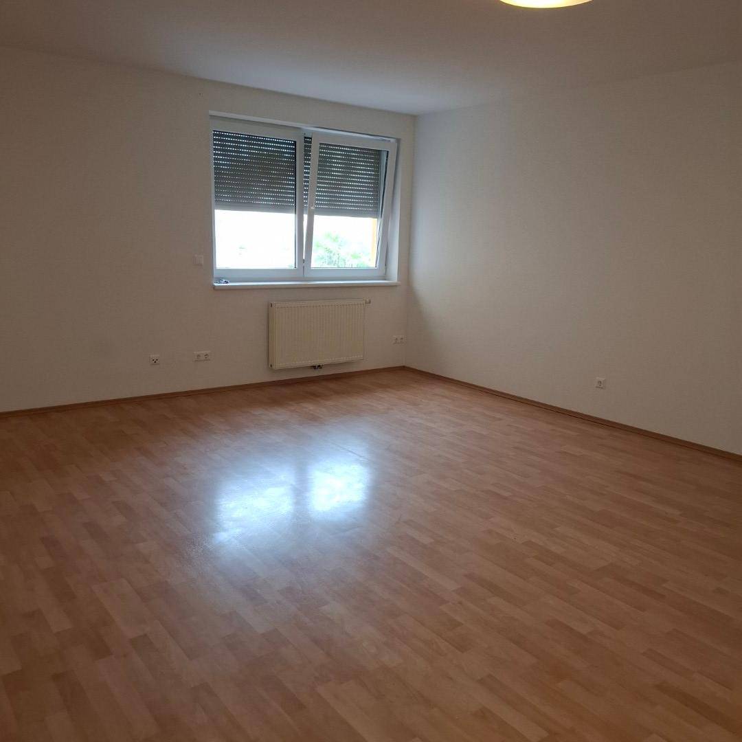 Heller, leerer Raum mit Laminatboden, weißen Wänden und einem Fenster mit Jalousien.