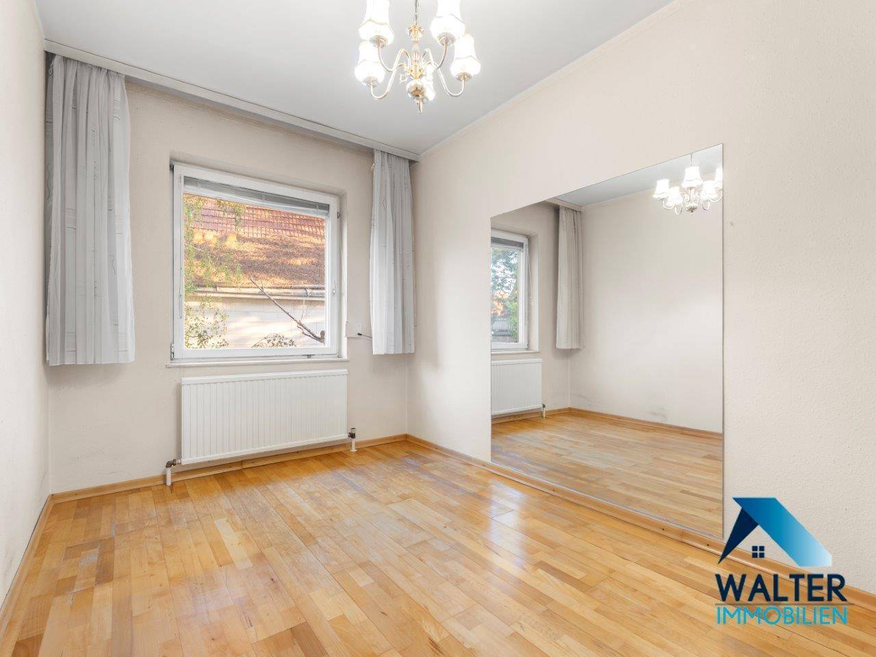 Helles Zimmer mit Parkettboden und großem Wandspiegel, ideal als Schlafzimmer nutzbar.