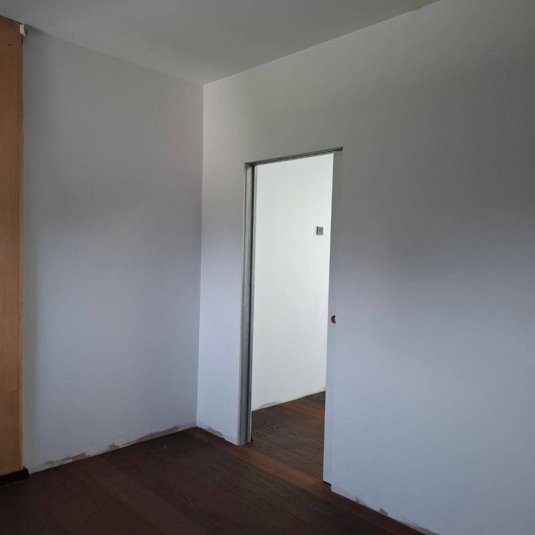 Helles Zimmer mit weiß gestrichenen Wänden und dunklem Holzboden, bereit zum Einzug.