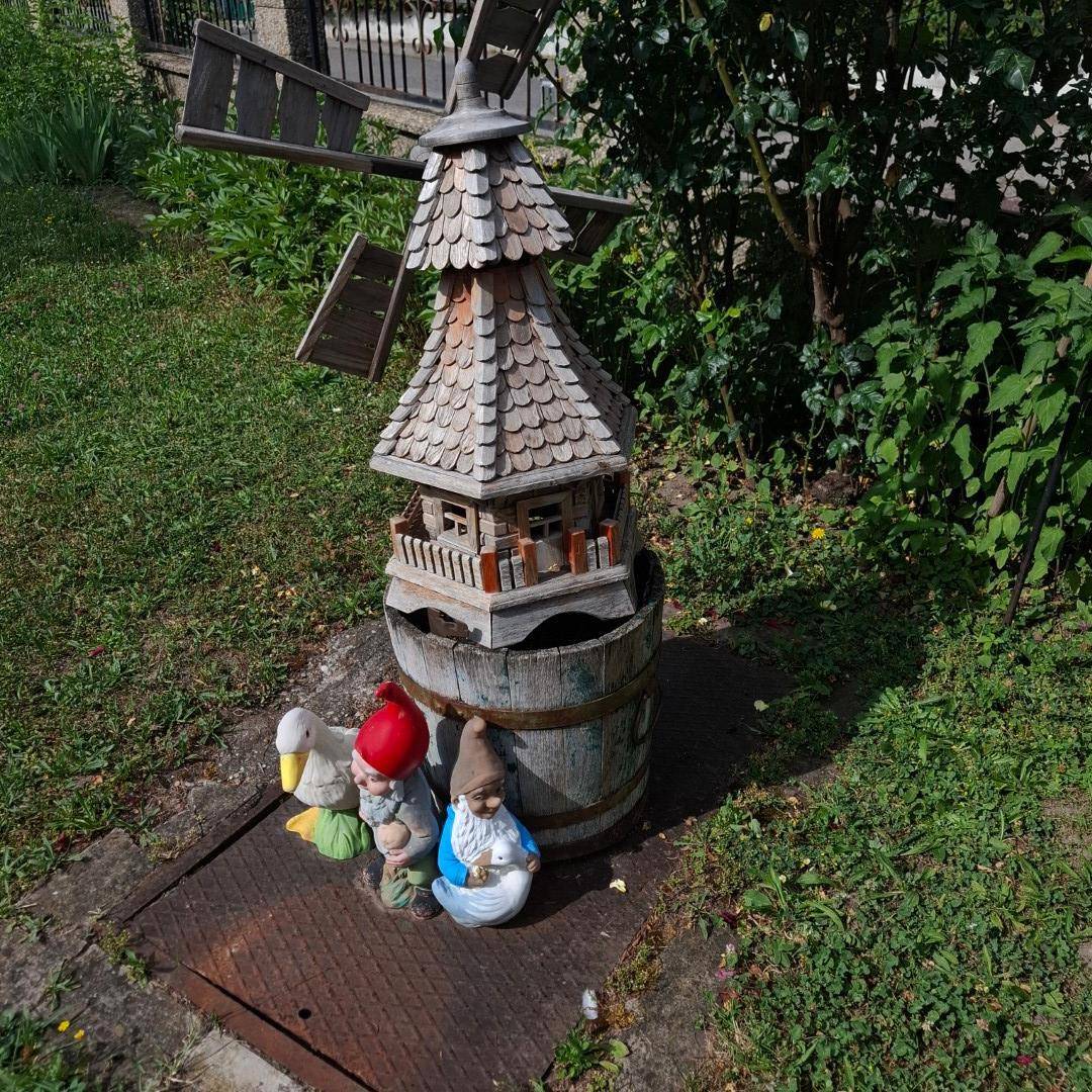 Detailaufnahme einer dekorativen Windmühle mit Gartenzwergen, die den Garten schmücken.