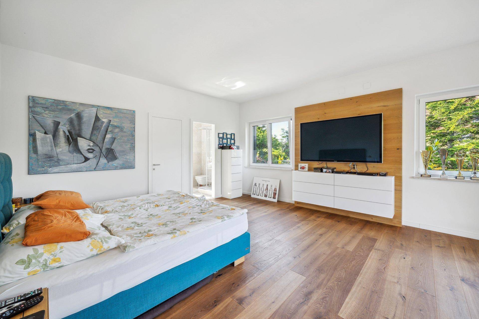 Helles Schlafzimmer mit Holzboden, großem Bett und Wandverkleidung für den Fernseher.