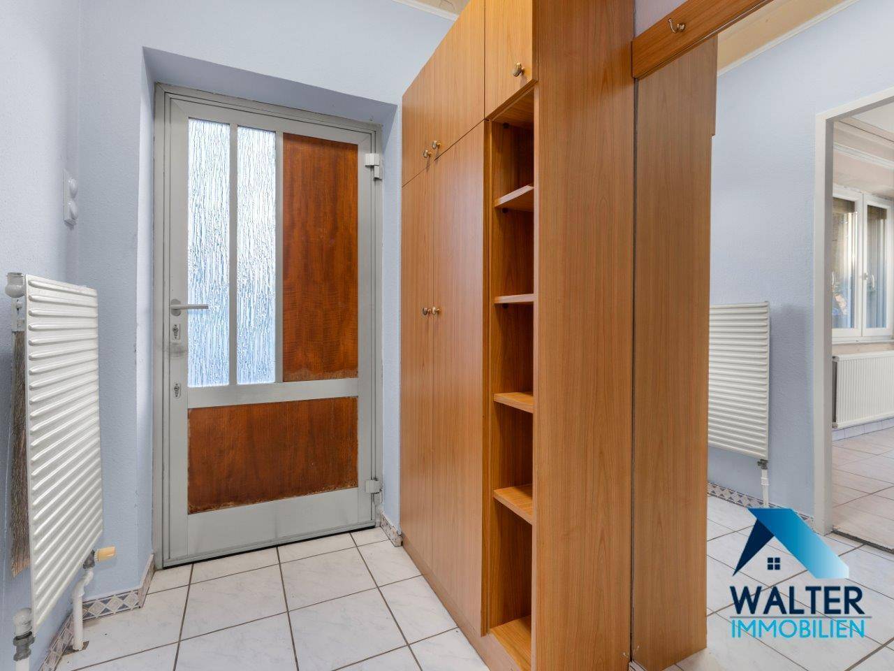 Eingangsbereich mit Fliesenboden und Holzschrank, der viel Stauraum bietet.