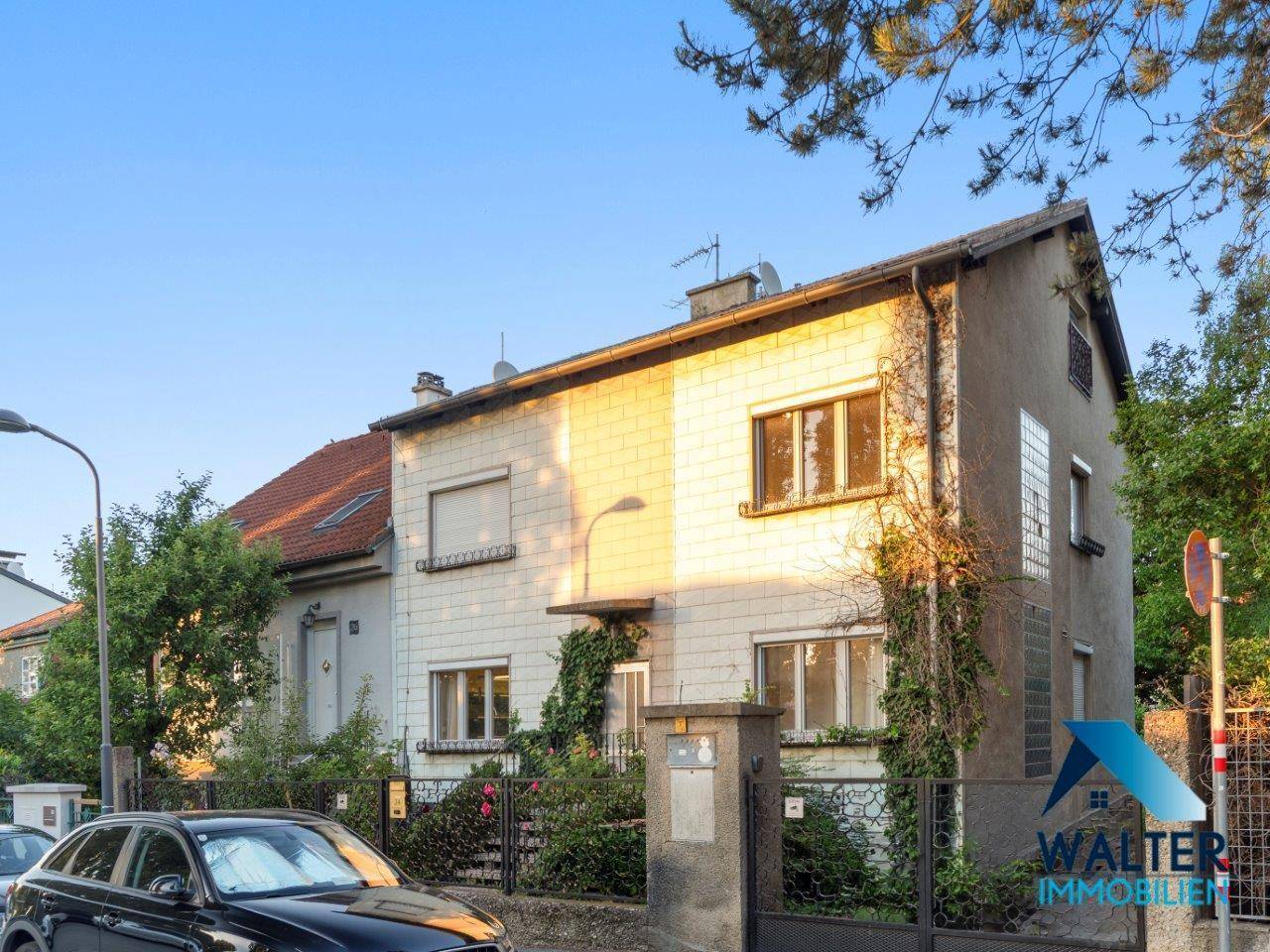 Fassade eines Mehrfamilienhauses mit hellen Steinplatten und grüner Bepflanzung.
