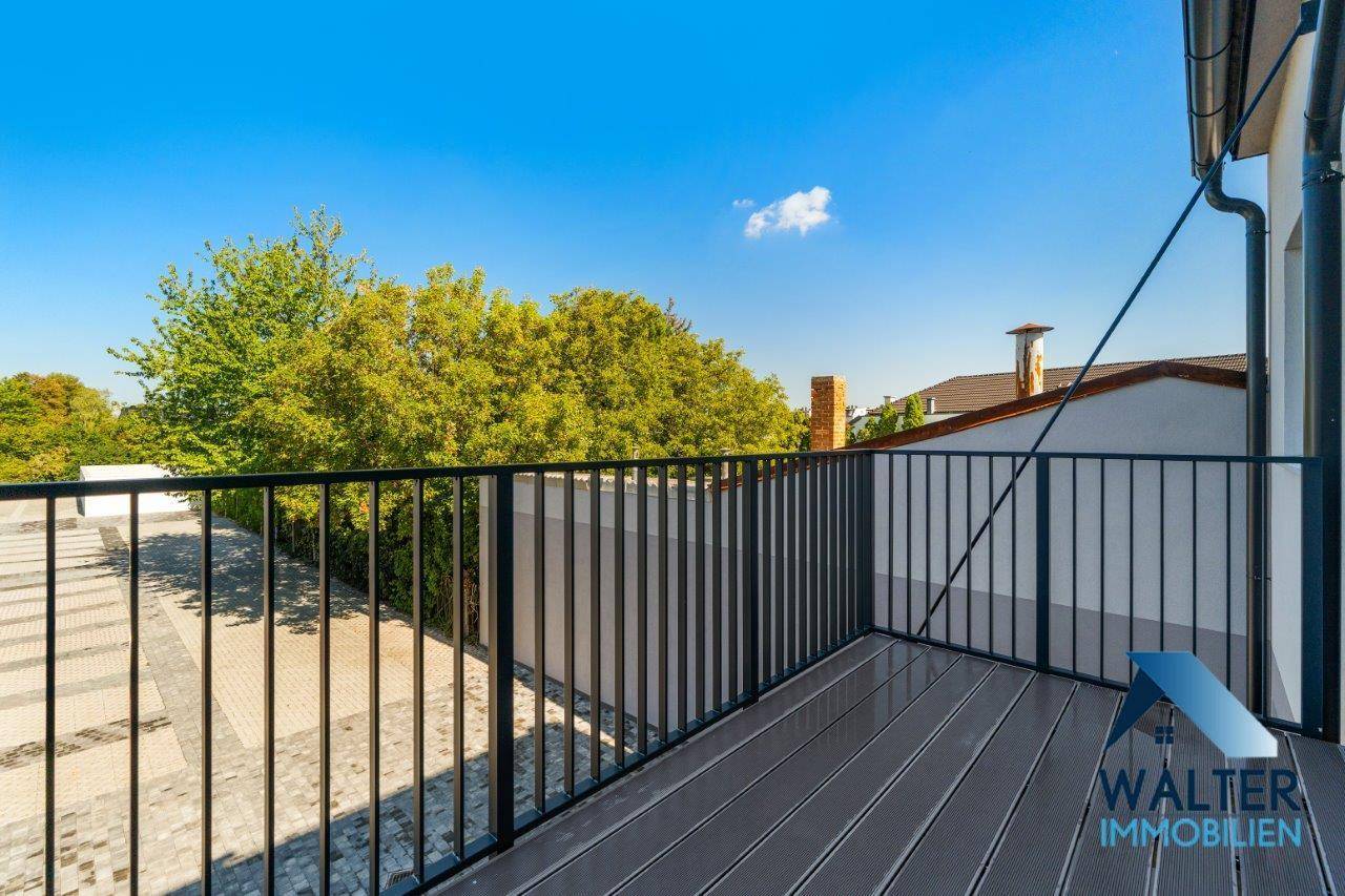 Geräumiger Balkon mit Holzdielenboden und schwarzem Metallgeländer, umgeben von Bäumen.