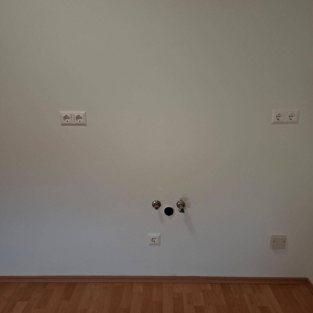 Detailansicht der Wand mit Steckdosen und Wasseranschlüssen, bereit für die Kücheninstallation.