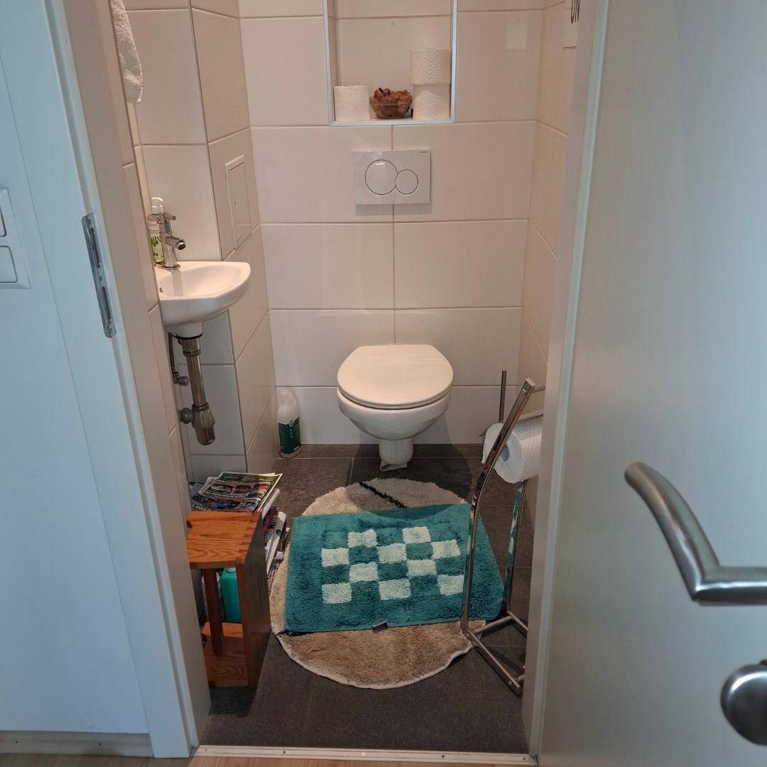 Kleines Gäste-WC mit wandhängender Toilette, kleinem Waschbecken und weißen Fliesen für einfache Pflege.