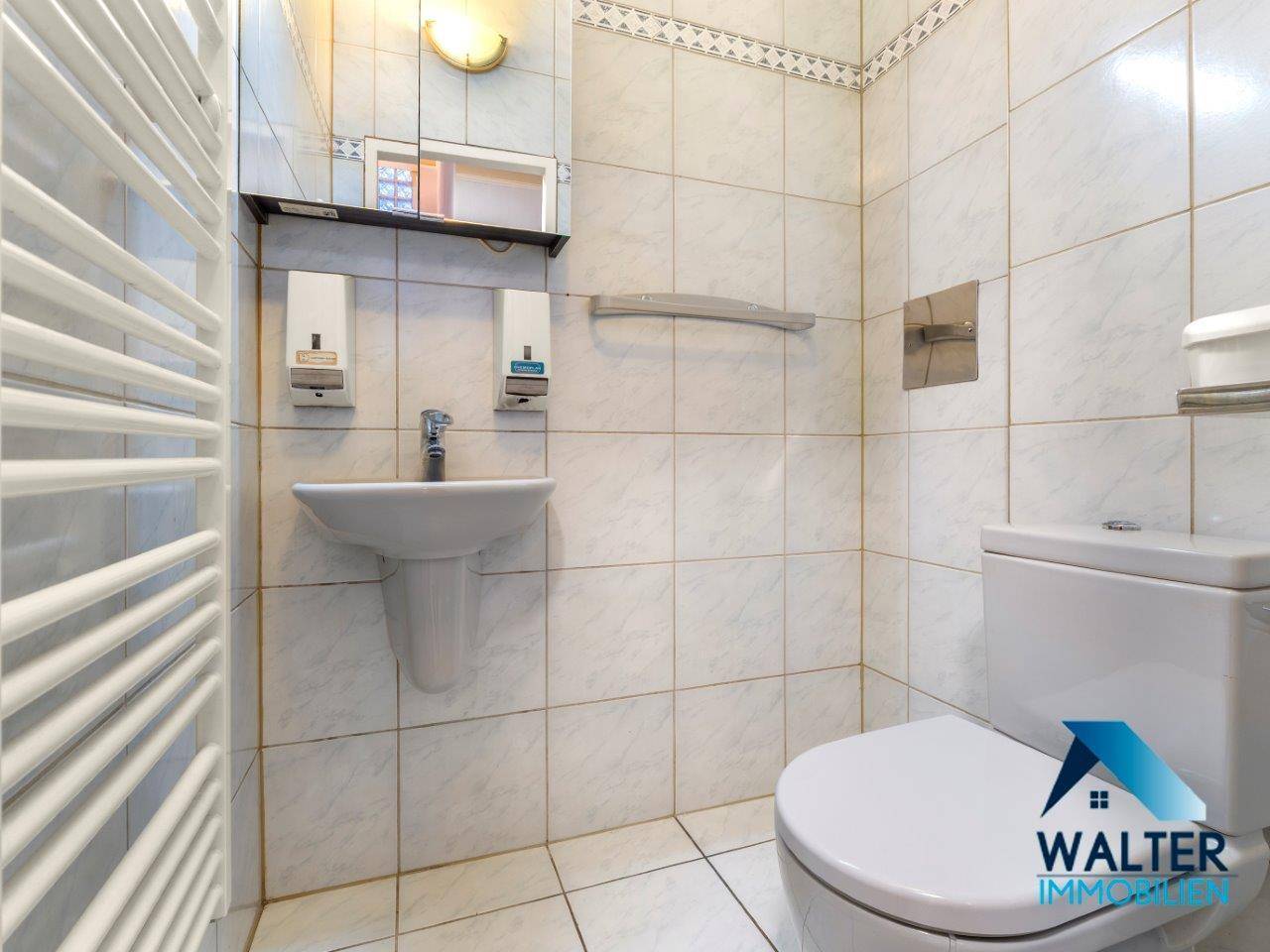 Kleines Gäste-WC mit weißen Fliesen, Waschbecken und beheiztem Handtuchhalter.