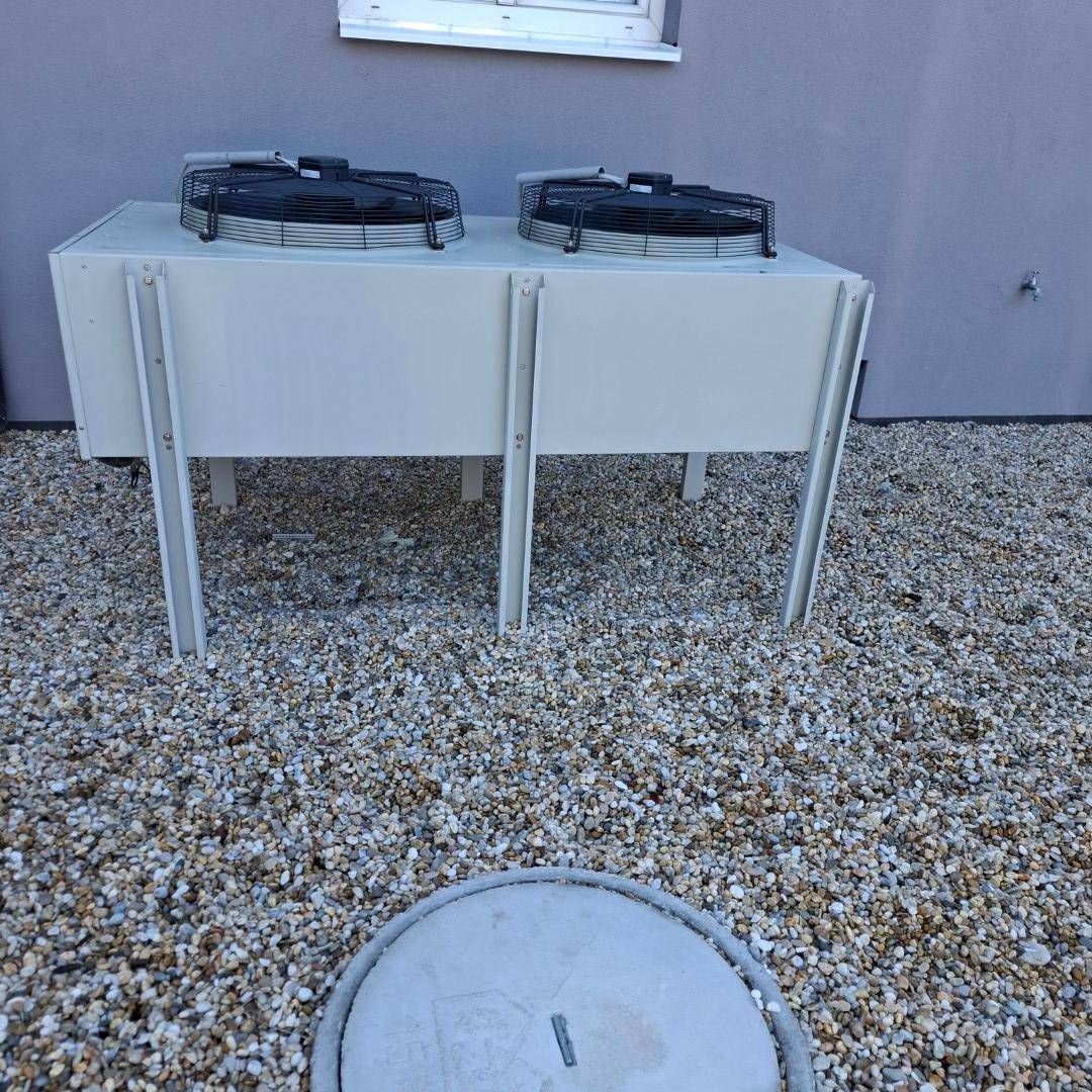 Außeneinheit einer Klimaanlage oder Wärmepumpe auf einem Kiesbett neben dem Gebäude.