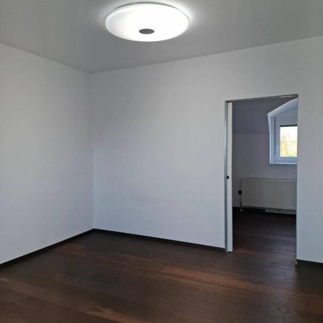 Geräumiges Zimmer mit dunklem Holzboden und Blick in einen angrenzenden Raum.