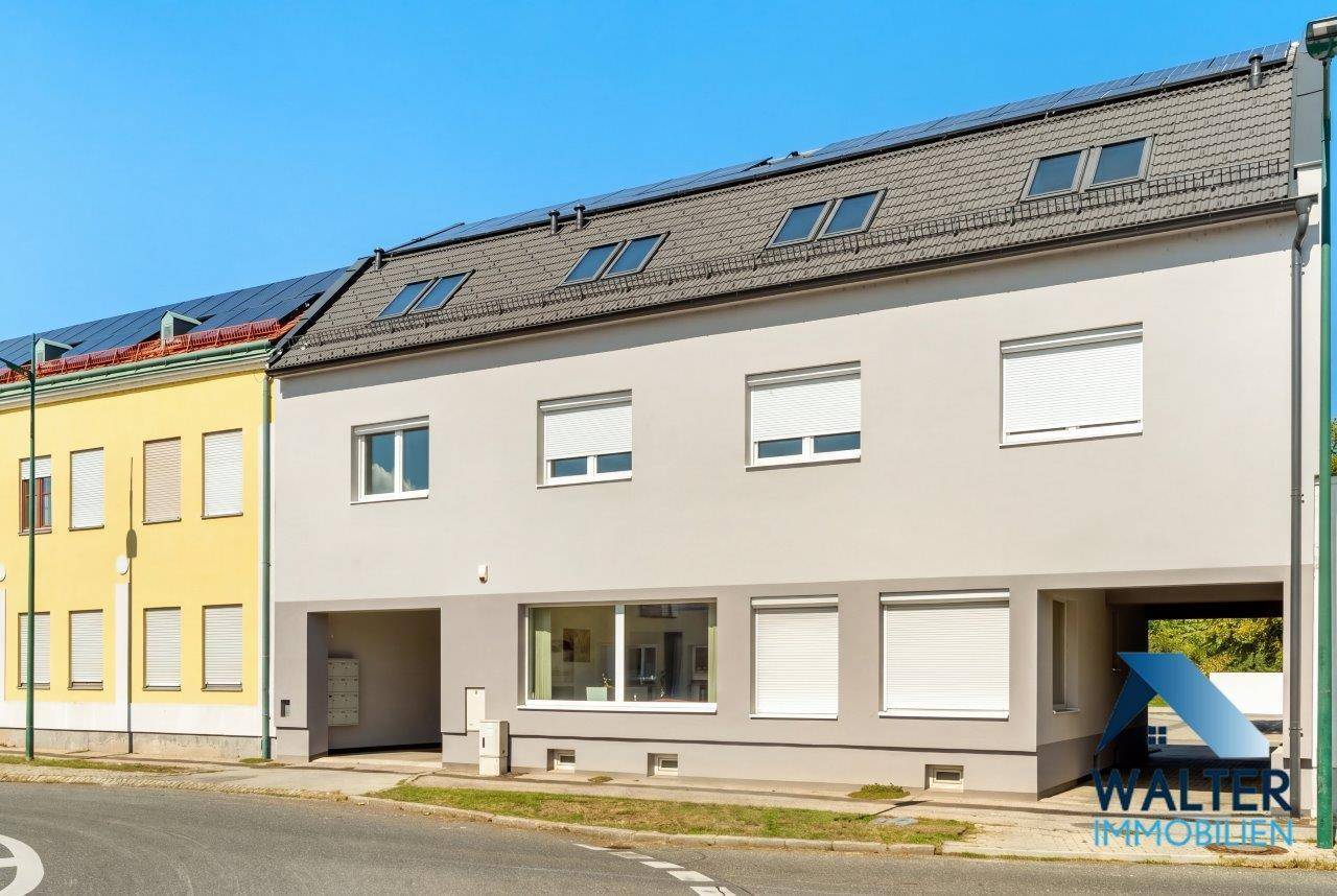 Fassade eines modernen Gebäudes mit großen Fenstern, Rollläden und einem überdachten Eingangsbereich.