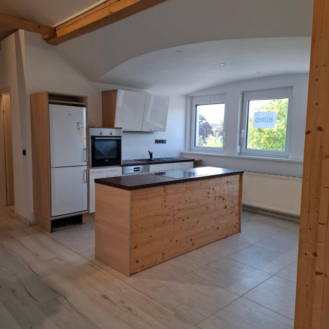 Moderne Küche mit Kochinsel, Holzelementen, weißen Schränken und Blick ins Grüne.