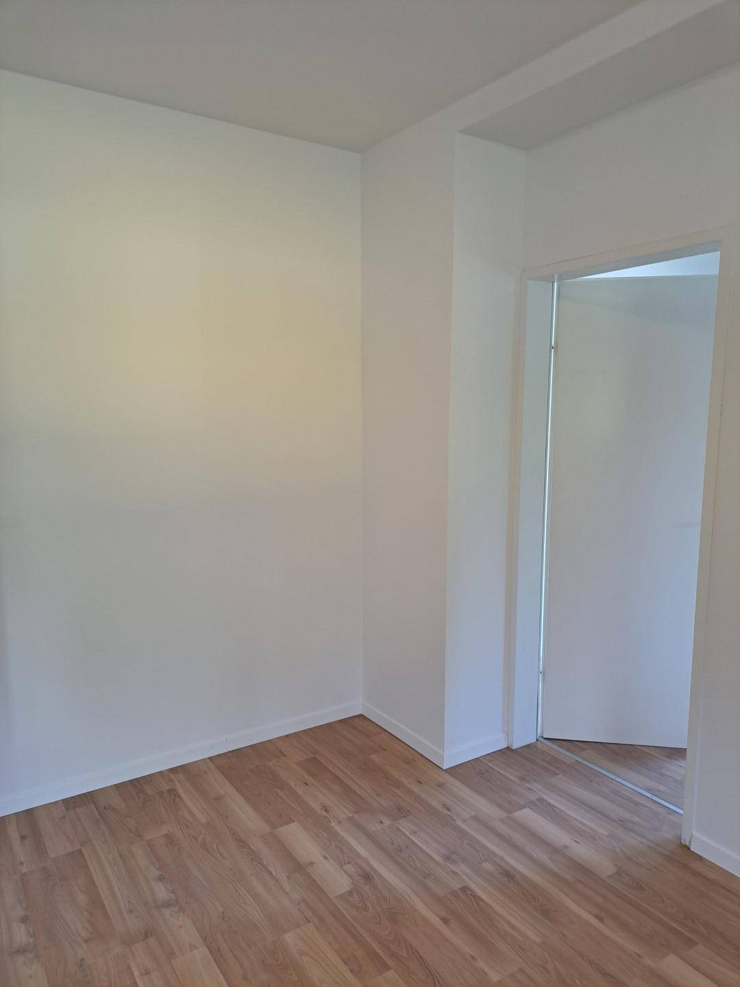 Leerer Raum mit Laminatboden und weiß gestrichenen Wänden, bereit zur Einrichtung.