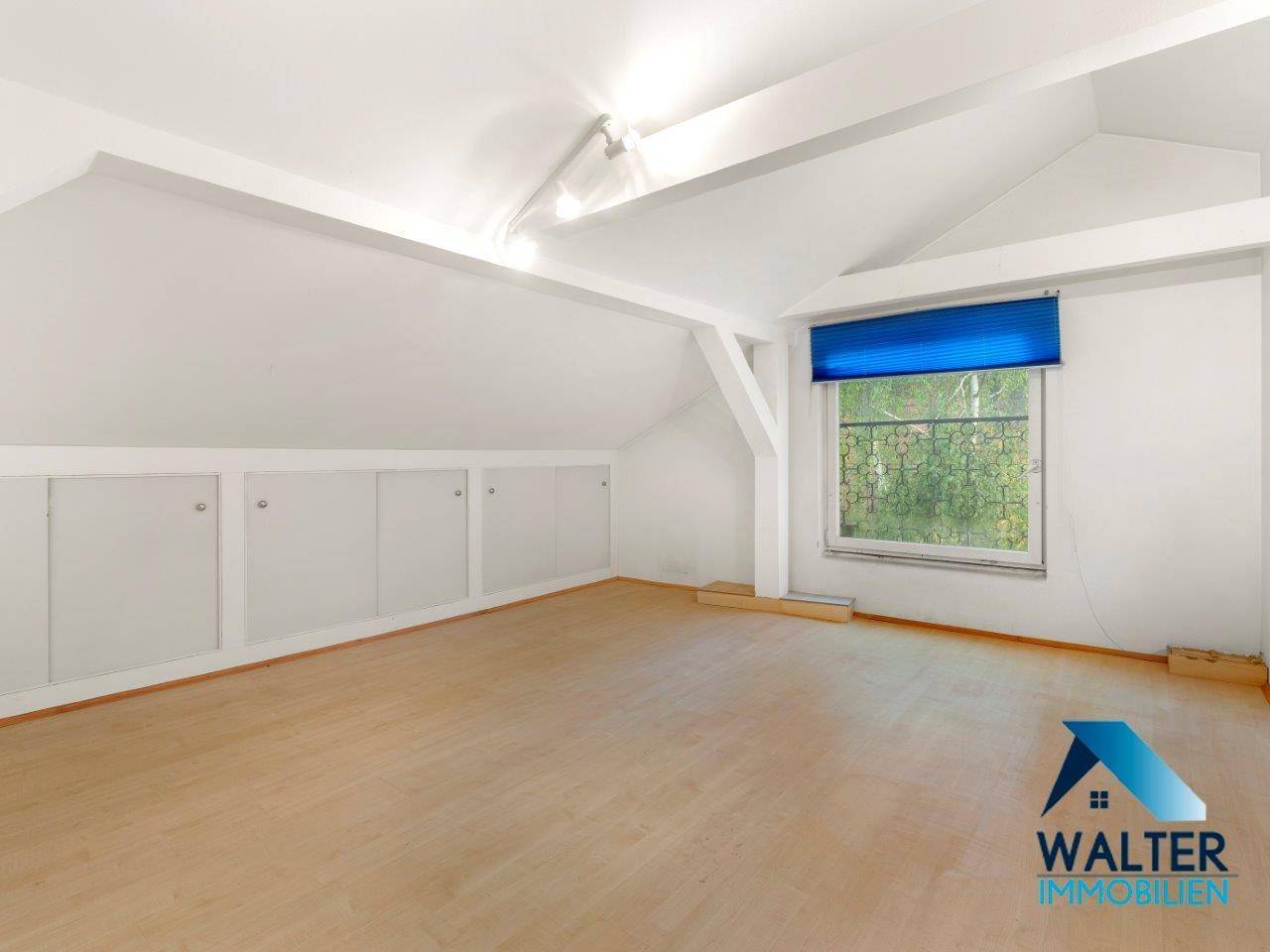 Helles Dachzimmer mit Holzboden, Dachschrägen und integrierten Stauräumen.