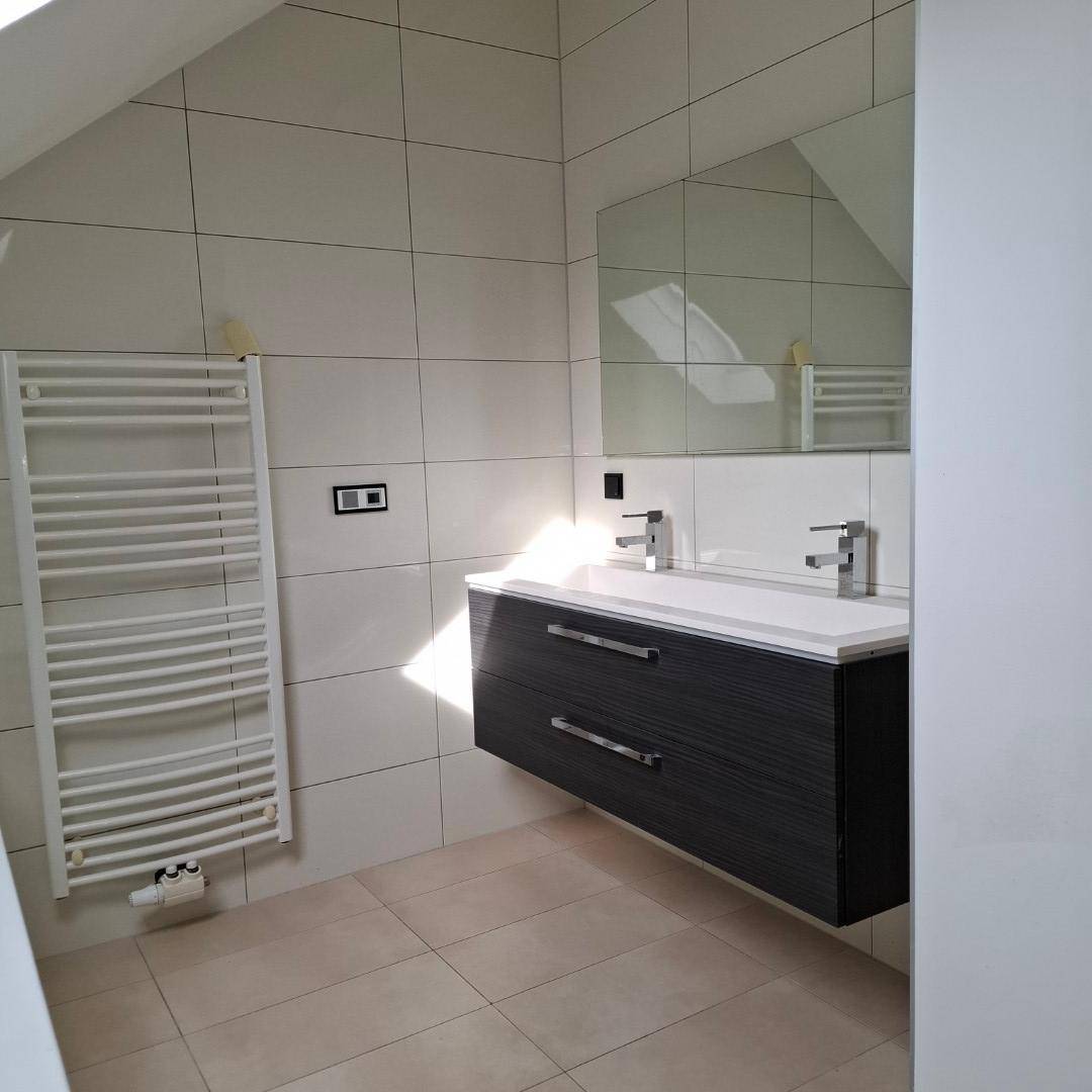 Modernes Badezimmer mit Waschtischunterschrank, großem Spiegel und Handtuchheizkörper unter einer Dachschräge.