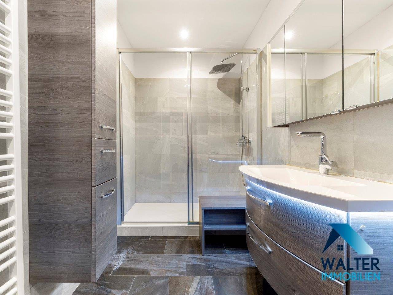 Modernes Badezimmer mit begehbarer Dusche, stilvollem Waschtisch und dunklen Fliesen.