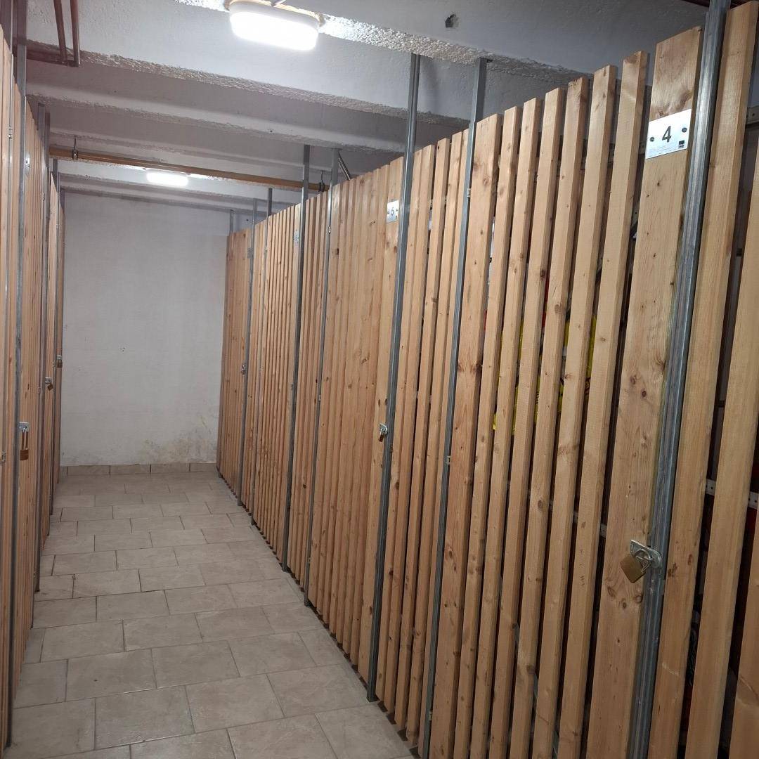 Reihe von Kellerabteilen mit Holztüren und Fliesenboden in einem gut beleuchteten Gang.