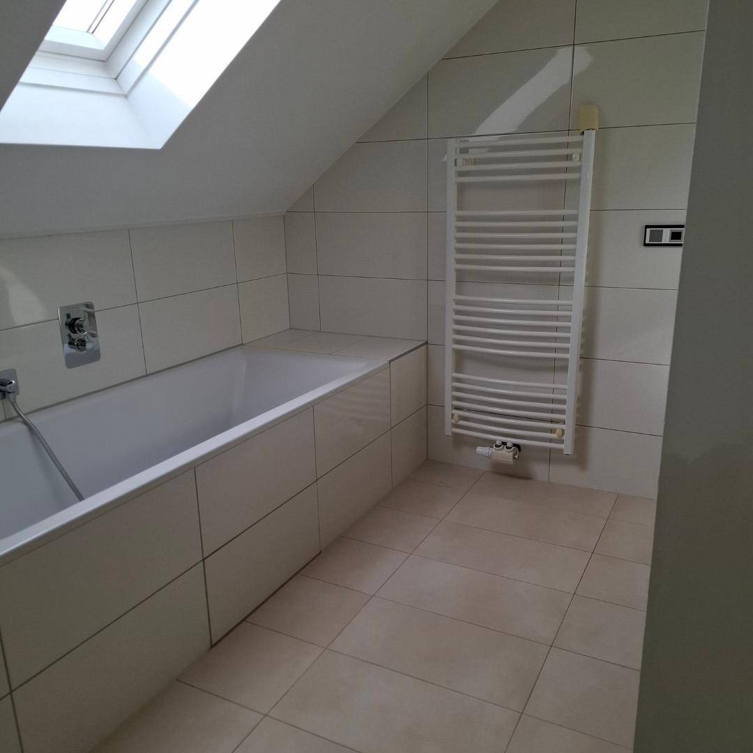 Badezimmer mit Badewanne, Handtuchheizkörper und Dachfenster unter einer Dachschräge, hell gefliest.