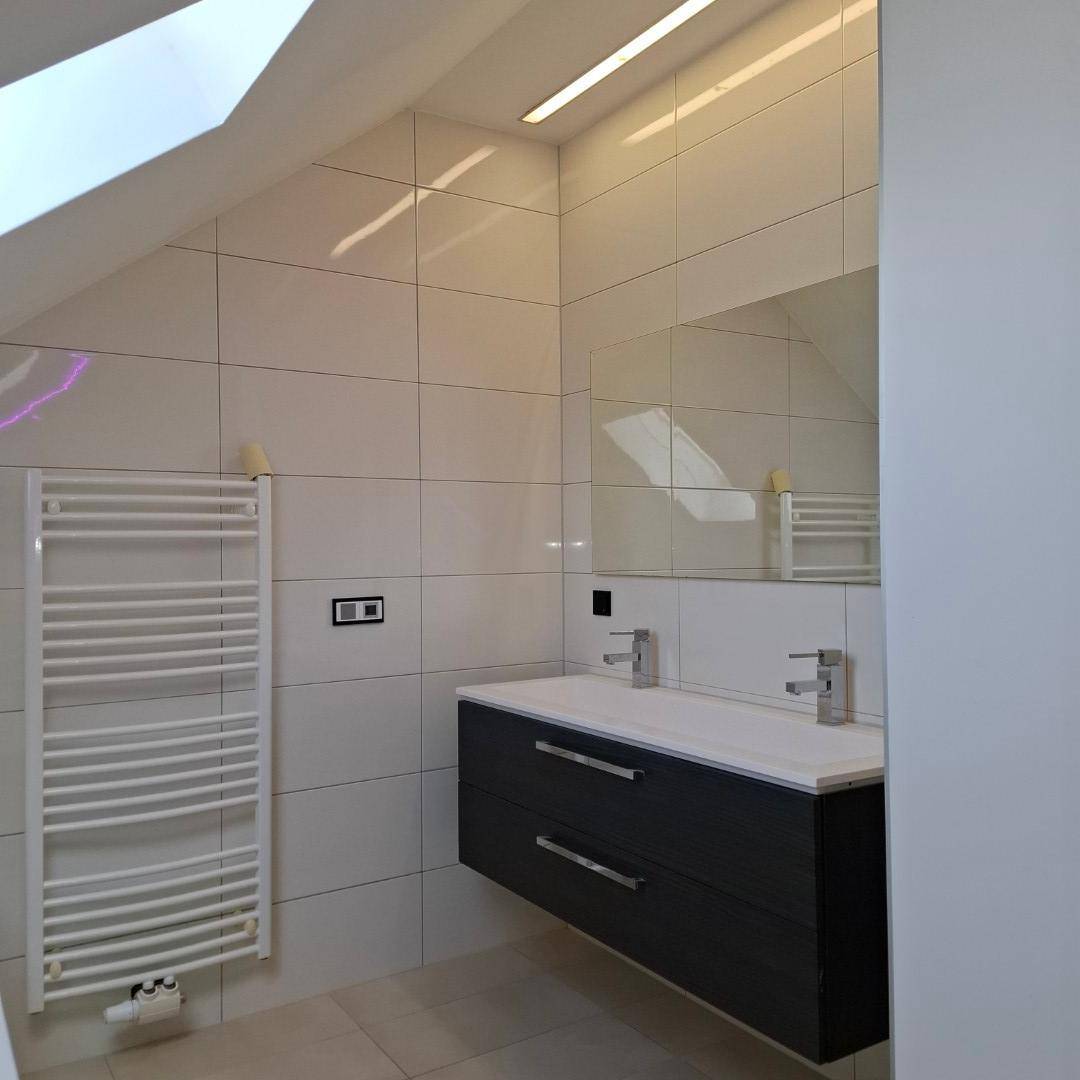 Modernes Badezimmer mit Waschtischunterschrank, großem Spiegel und Handtuchheizkörper unter einer Dachschräge.