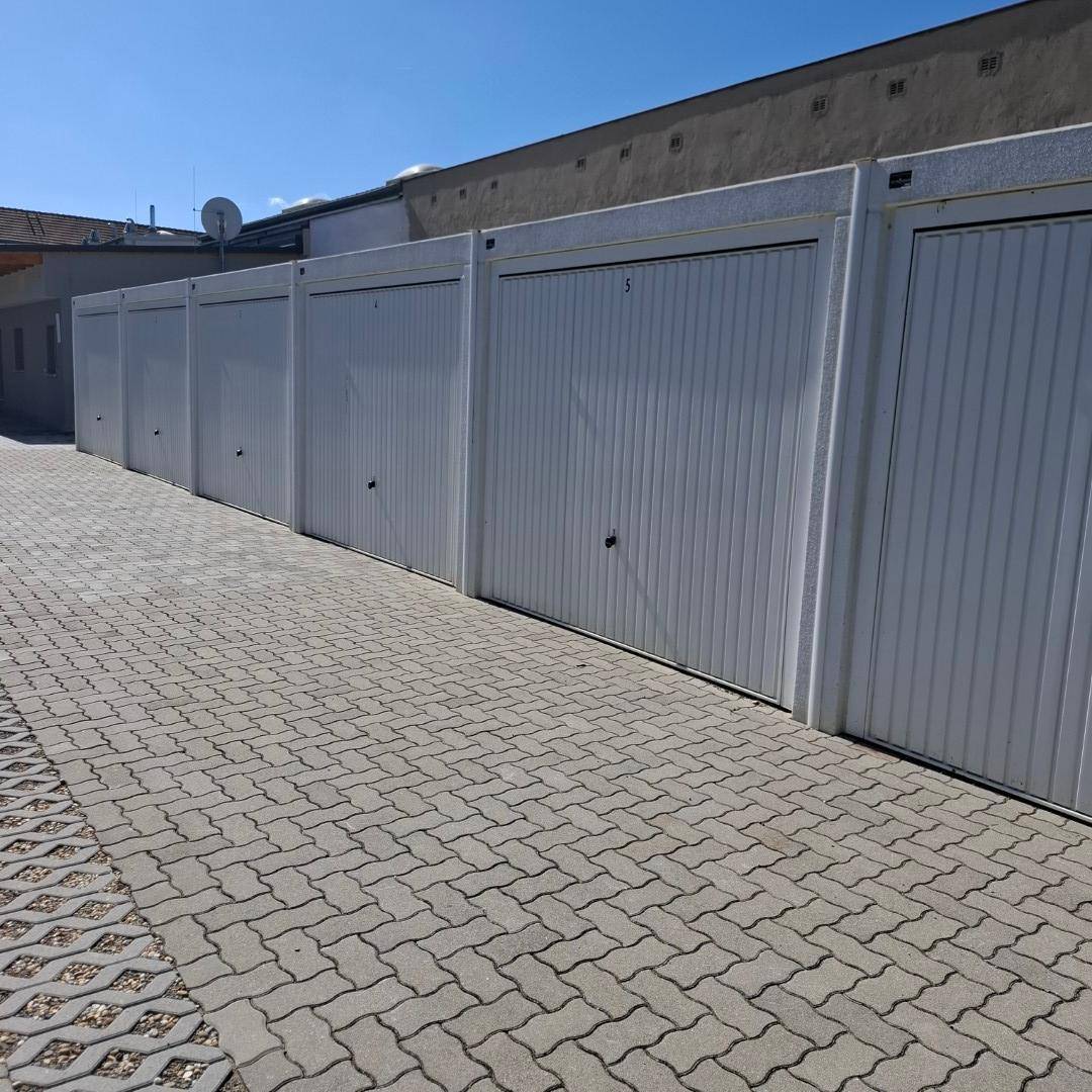 Reihe von Garagenboxen mit weißen Toren und einem gepflasterten Zufahrtsbereich.