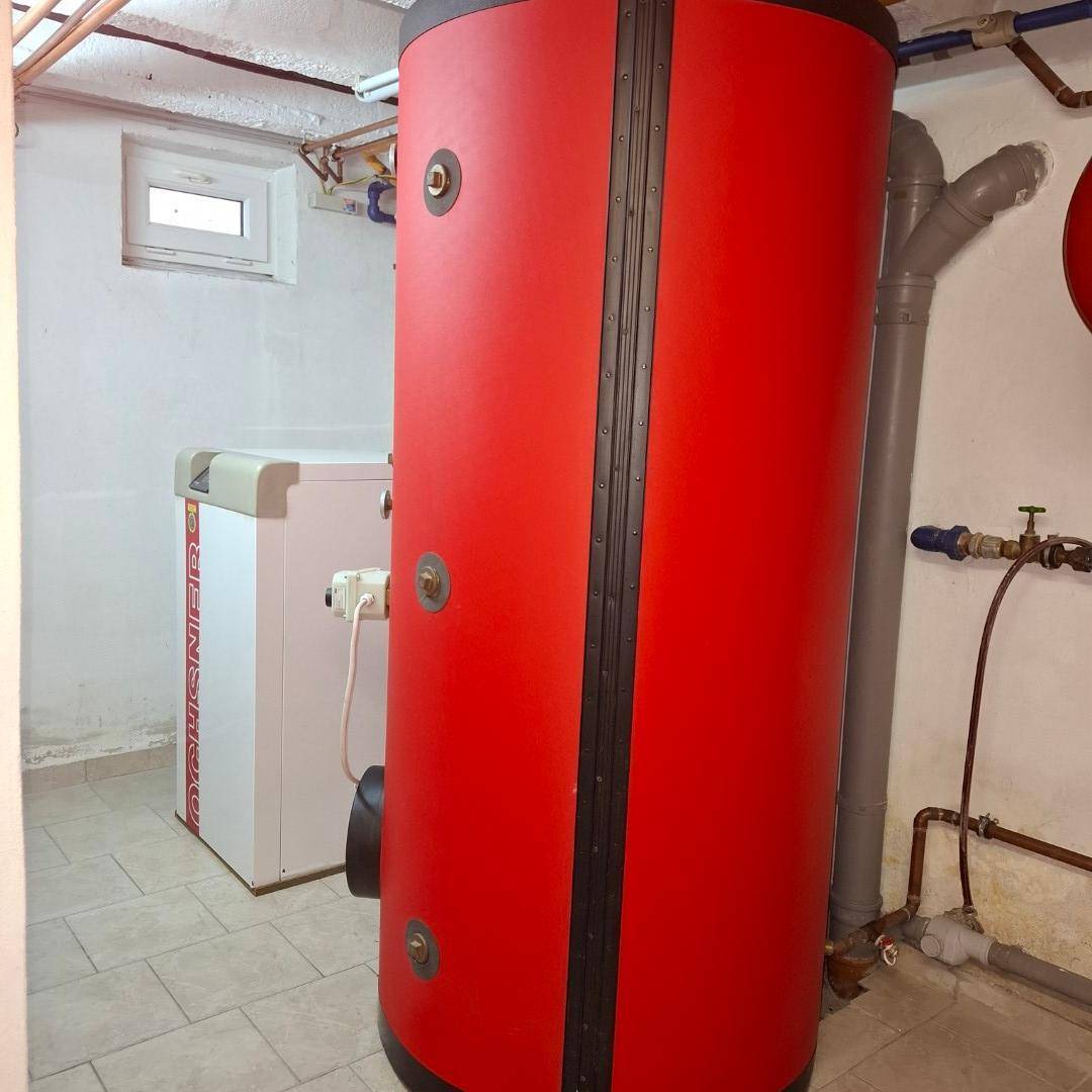 Heizungsraum im Keller mit einem großen roten Warmwasserspeicher und einer Wärmepumpe.