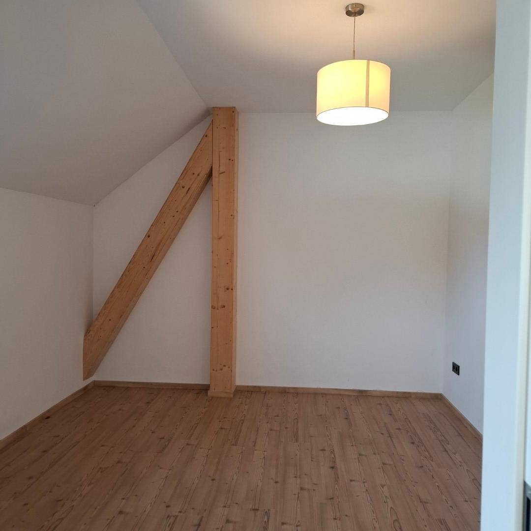 Helles Zimmer im Dachgeschoss mit Holzbalken, Dachschräge und Holzdielenboden.
