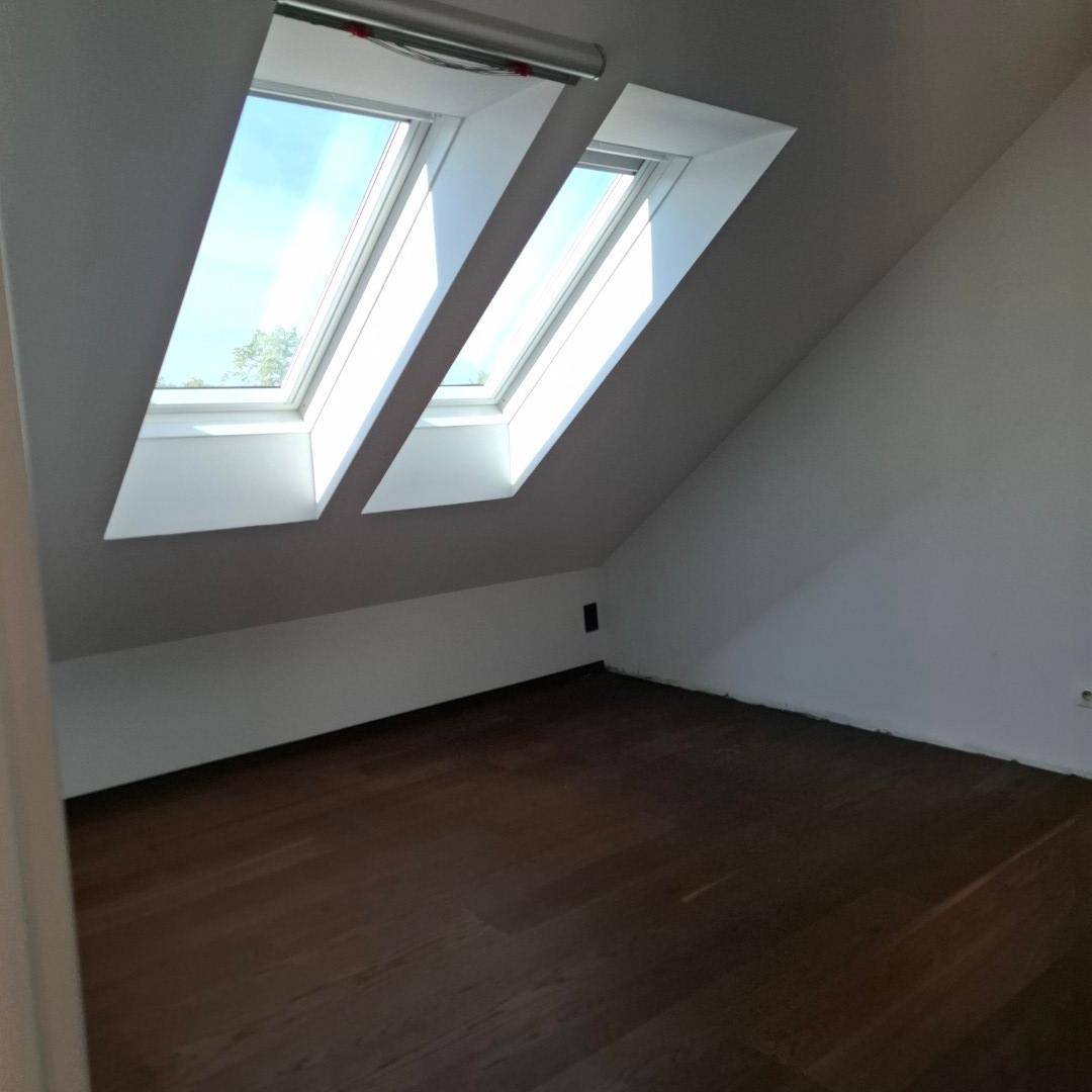 Helles Zimmer im Dachgeschoss mit zwei großen Dachfenstern und dunklem Holzboden.