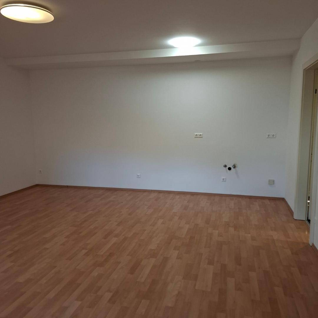 Heller Raum mit Laminatboden und weißen Wänden, vorbereitet für eine Küche mit sichtbaren Anschlüssen.