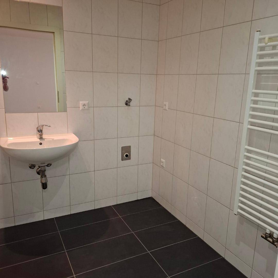 Modernes Badezimmer mit weißen Wandfliesen, dunklem Boden und einem praktischen Handtuchheizkörper.