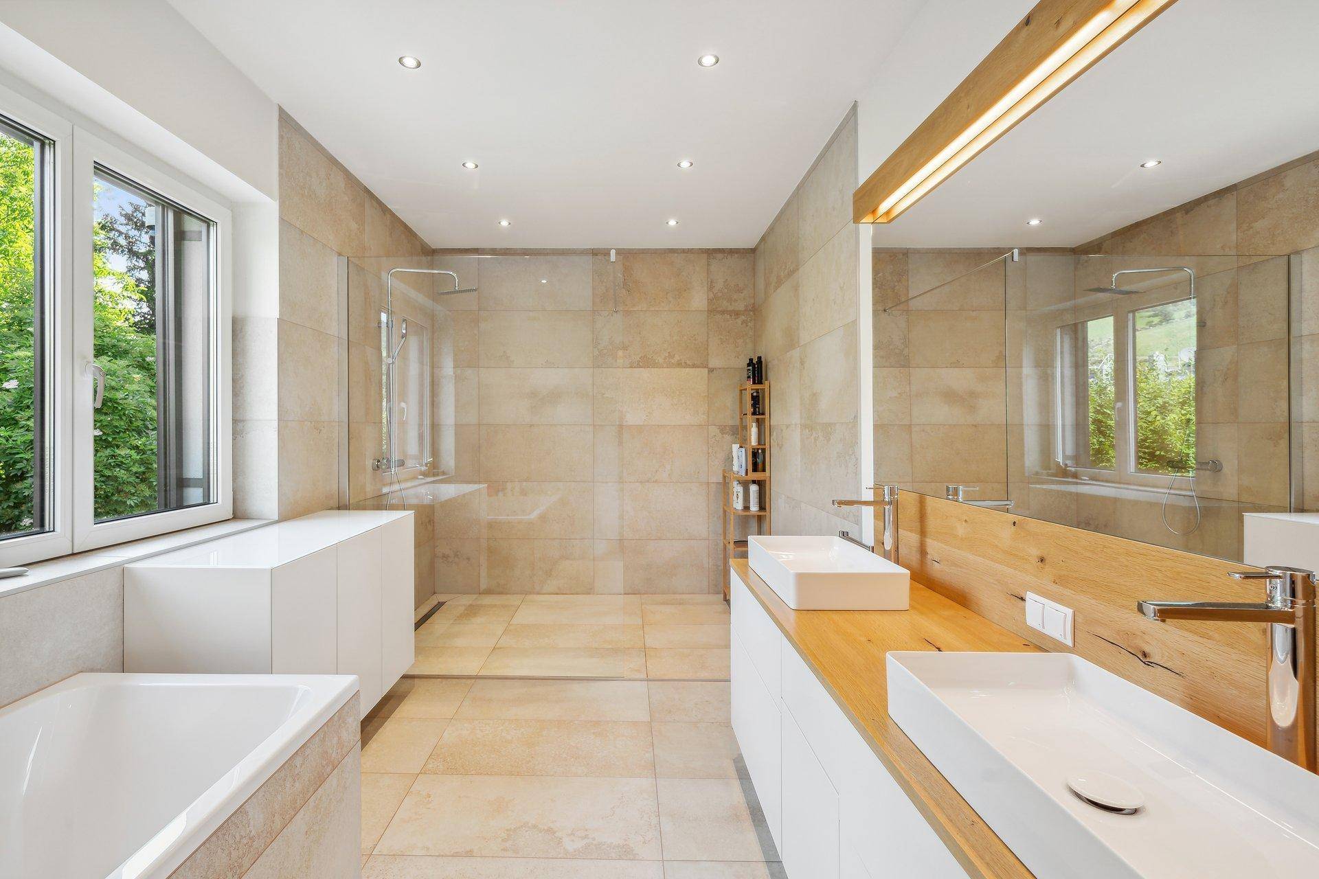 Modernes Badezimmer mit Doppelwaschbecken, großer Dusche und Badewanne, hell durch Fenster.