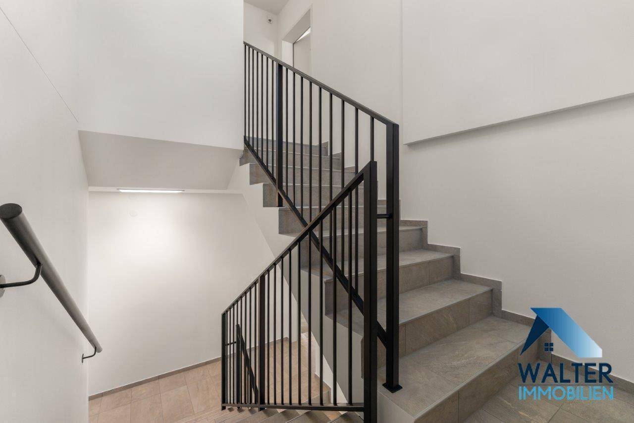 Modernes Treppenhaus mit gefliesten Stufen und schwarzem Metallgeländer in einem Neubau.