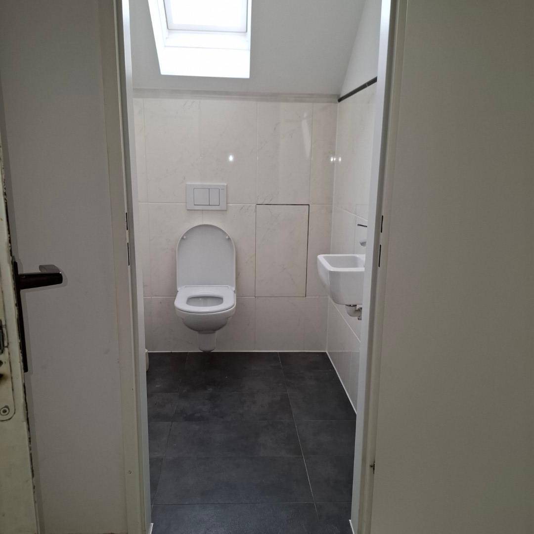 Modernes Gäste-WC mit wandhängendem WC, kleinem Waschbecken und Dachfenster für natürliches Licht.