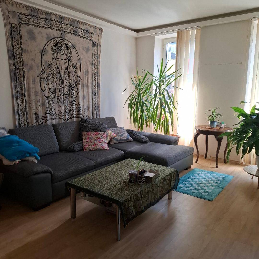 Gemütliches Wohnzimmer mit großem Ecksofa, Pflanzen und dekorativem Wandteppich, der eine persönliche Note verleiht.